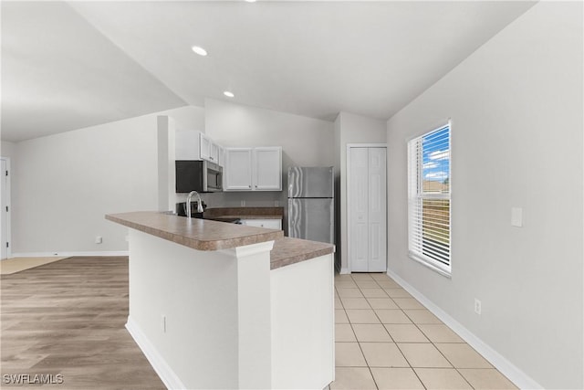 kitchen featuring lofted ceiling, appliances with stainless steel finishes, white cabinets, a peninsula, and baseboards