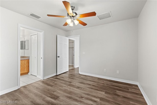 unfurnished bedroom with baseboards, visible vents, wood finished floors, and ensuite bathroom