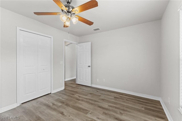 unfurnished bedroom with a closet, visible vents, a ceiling fan, wood finished floors, and baseboards