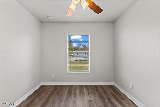 empty room with dark wood-style floors, a ceiling fan, and baseboards