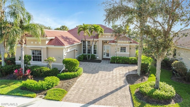 mediterranean / spanish home featuring a garage, a tiled roof, decorative driveway, and stucco siding