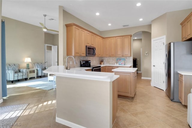 kitchen with a peninsula, stainless steel appliances, a sink, light countertops, and light brown cabinetry