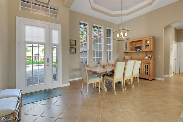 dining room with arched walkways, a tray ceiling, light tile patterned floors, an inviting chandelier, and baseboards