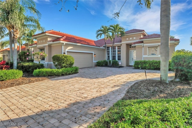 mediterranean / spanish-style home with a tiled roof, decorative driveway, an attached garage, and stucco siding