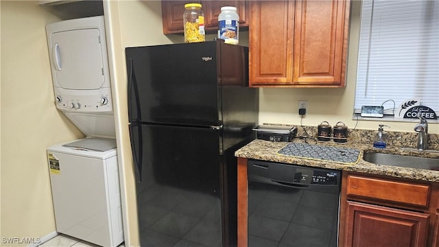 kitchen with stacked washer / drying machine, black appliances, sink, stone counters, and light tile patterned flooring