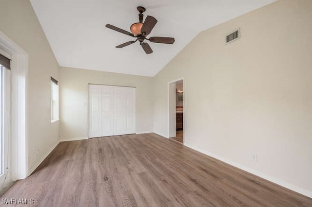 unfurnished bedroom with multiple windows, lofted ceiling, a closet, and light wood-type flooring