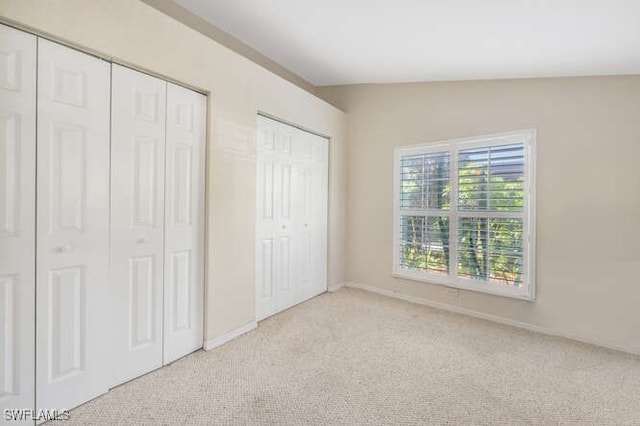 unfurnished bedroom with multiple closets, vaulted ceiling, and light colored carpet