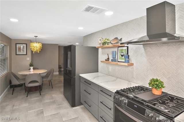 kitchen featuring light stone countertops, visible vents, gray cabinets, range with gas cooktop, and wall chimney exhaust hood