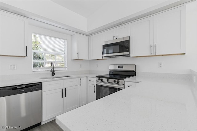 kitchen featuring appliances with stainless steel finishes, white cabinetry, sink, hardwood / wood-style flooring, and light stone countertops