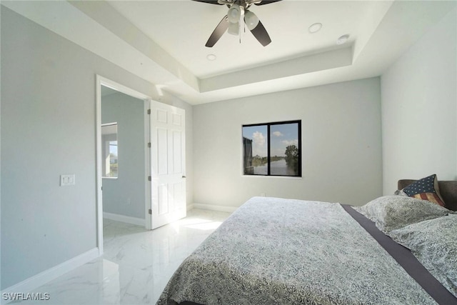 bedroom with multiple windows, a tray ceiling, and ceiling fan