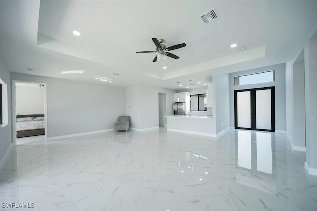 unfurnished living room with french doors, ceiling fan, and a tray ceiling