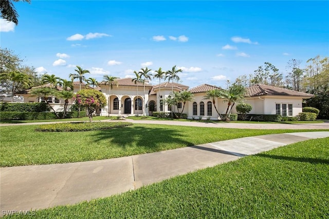 mediterranean / spanish home with a front yard, a tile roof, and stucco siding