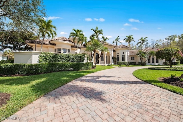 mediterranean / spanish-style home featuring a tiled roof, decorative driveway, a front yard, and stucco siding