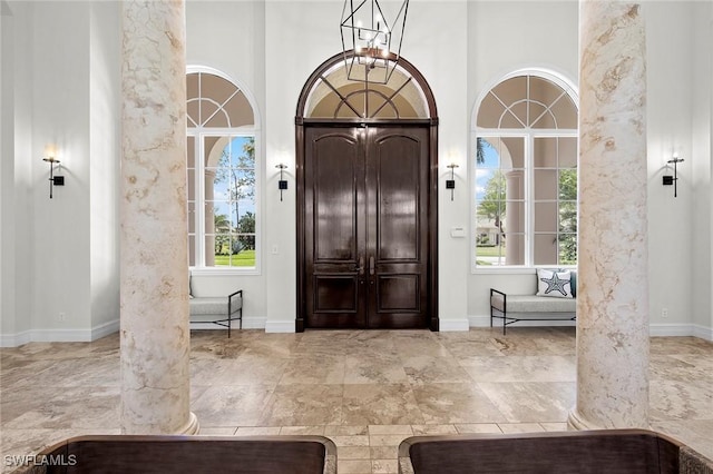 foyer featuring a towering ceiling, ornate columns, baseboards, and an inviting chandelier