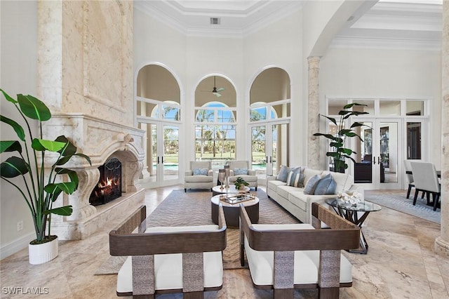 living area featuring french doors, crown molding, a towering ceiling, a premium fireplace, and ornate columns