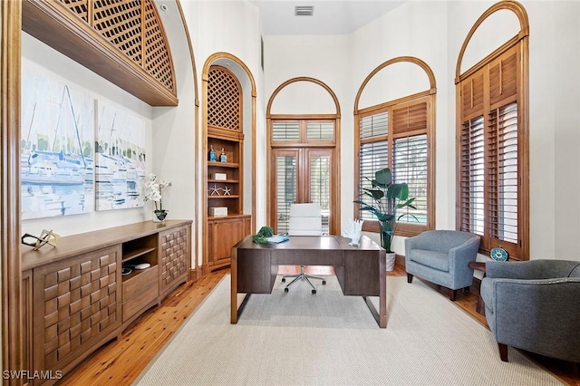 home office featuring visible vents, built in shelves, a high ceiling, and light wood-style flooring