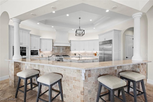 kitchen with stainless steel appliances, a tray ceiling, custom range hood, and a large island with sink