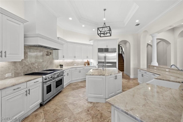 kitchen with premium appliances, a sink, an island with sink, a raised ceiling, and custom range hood