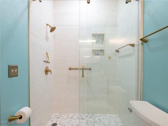 bathroom featuring a shower with door and toilet