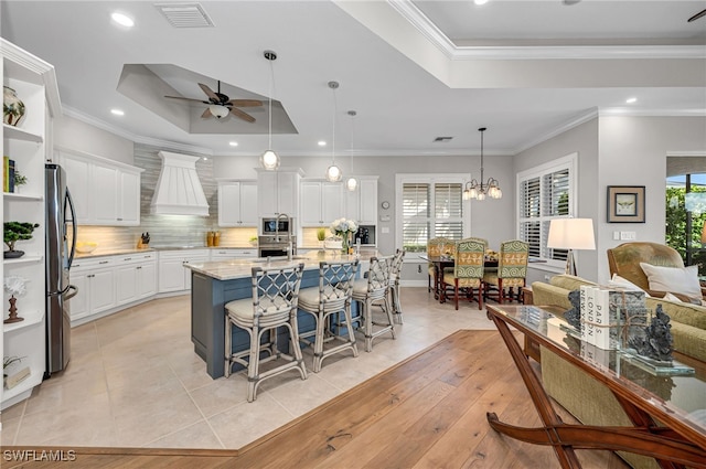 kitchen with white cabinets, a kitchen island with sink, stainless steel appliances, a raised ceiling, and light stone countertops