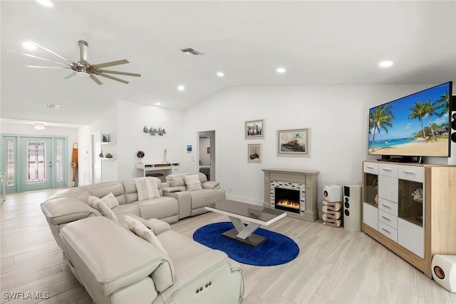 living room with vaulted ceiling, a warm lit fireplace, visible vents, light wood-style floors, and ceiling fan