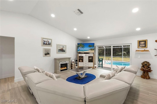 living area featuring recessed lighting, vaulted ceiling, visible vents, and a glass covered fireplace