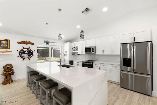 kitchen featuring white cabinetry, lofted ceiling, a center island with sink, a sink, and appliances with stainless steel finishes