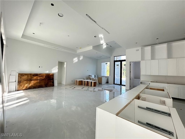 interior space featuring a tray ceiling, white cabinets, a high ceiling, and a spacious island