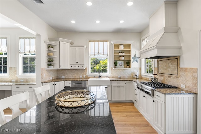 kitchen with white cabinets, dark stone counters, custom exhaust hood, stainless steel appliances, and open shelves