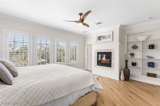 bedroom featuring visible vents, a tiled fireplace, ornamental molding, ceiling fan, and wood finished floors