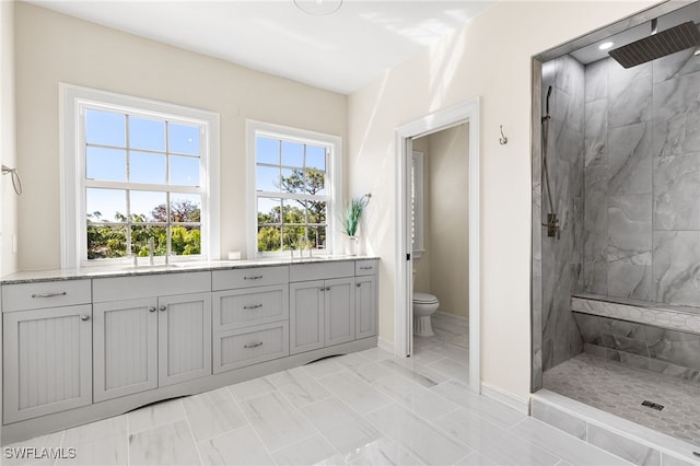 bathroom with baseboards, toilet, vanity, and a marble finish shower