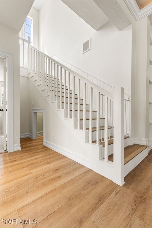 staircase featuring visible vents, a towering ceiling, baseboards, and wood finished floors