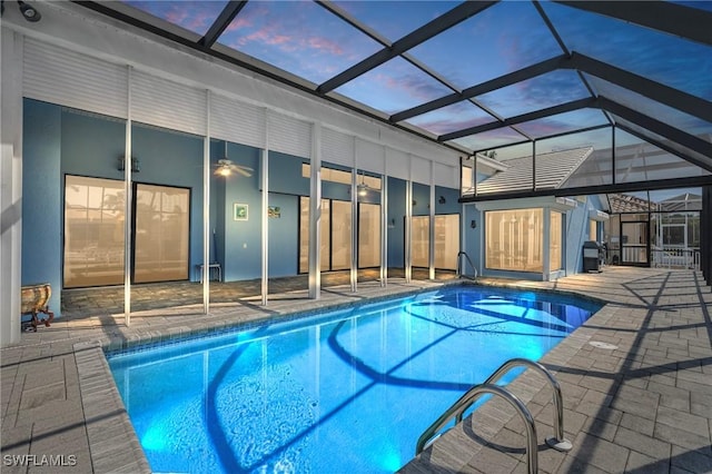 pool at dusk featuring ceiling fan, glass enclosure, and a patio