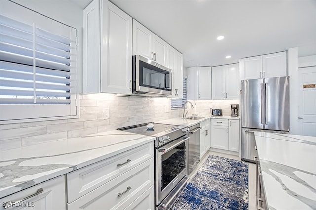 kitchen with sink, white cabinetry, backsplash, stainless steel appliances, and light stone countertops