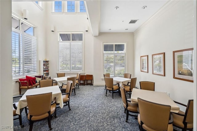 dining area with a high ceiling, ornamental molding, a wealth of natural light, and dark carpet