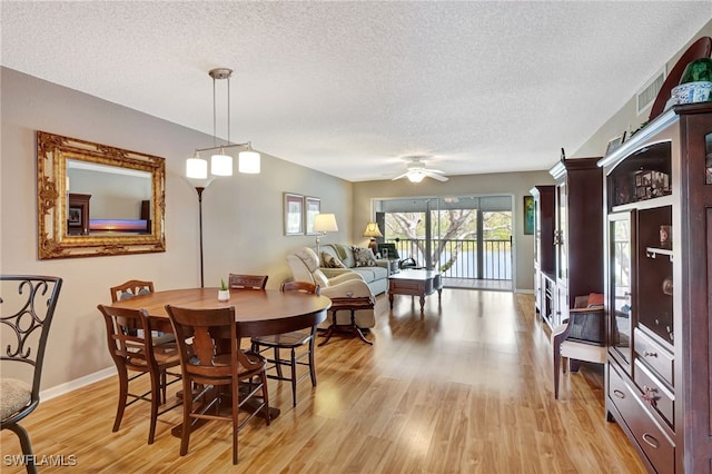 dining room with a textured ceiling, light wood-style flooring, visible vents, a ceiling fan, and baseboards