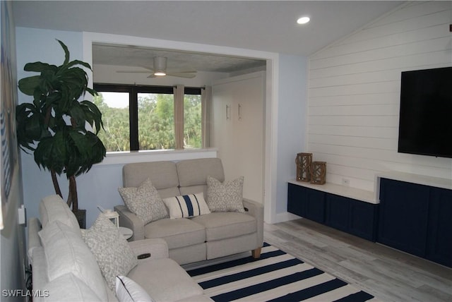 living room featuring ceiling fan, wood walls, lofted ceiling, and light wood-type flooring