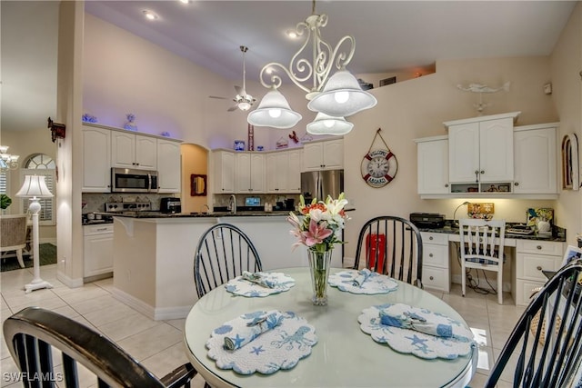 dining space featuring built in desk, visible vents, a towering ceiling, light tile patterned flooring, and ceiling fan with notable chandelier