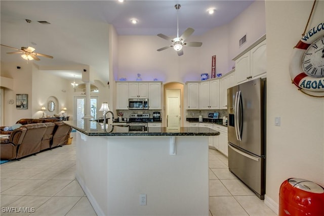 kitchen with light tile patterned floors, white cabinets, open floor plan, dark stone countertops, and stainless steel appliances