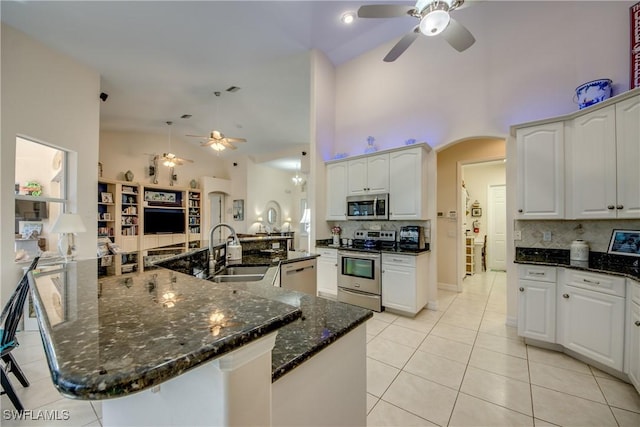 kitchen with dark stone countertops, stainless steel appliances, a peninsula, and white cabinetry