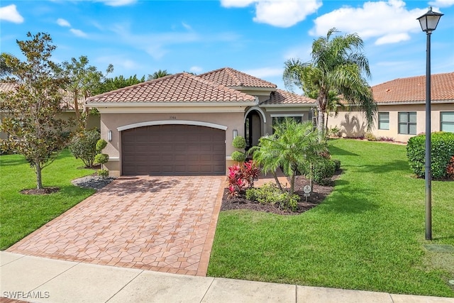 mediterranean / spanish home with decorative driveway, stucco siding, a front yard, a garage, and a tiled roof