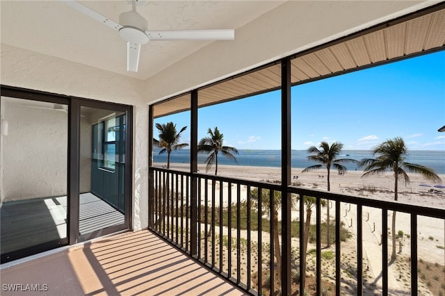 sunroom with ceiling fan, a water view, and a beach view