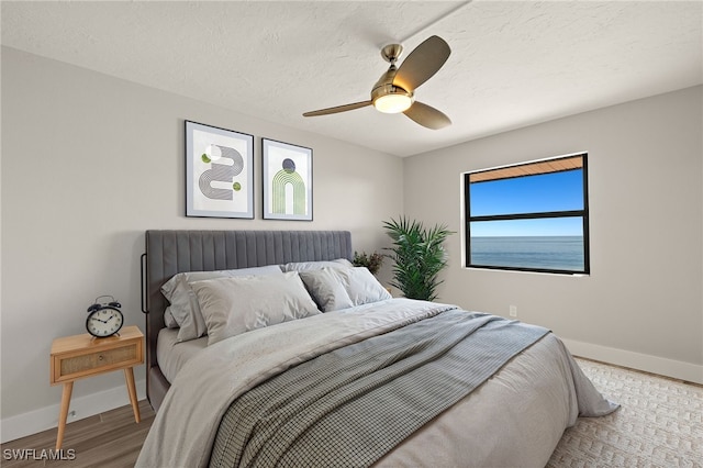 bedroom with light hardwood / wood-style flooring, ceiling fan, and a textured ceiling