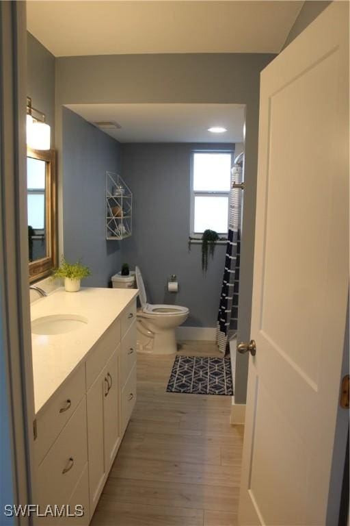 bathroom with curtained shower, toilet, wood finished floors, vanity, and baseboards