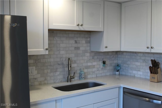 kitchen with a sink, white cabinetry, stainless steel dishwasher, and freestanding refrigerator