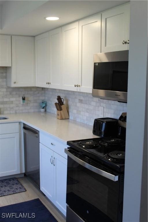 kitchen with white cabinetry, stainless steel appliances, backsplash, and light countertops