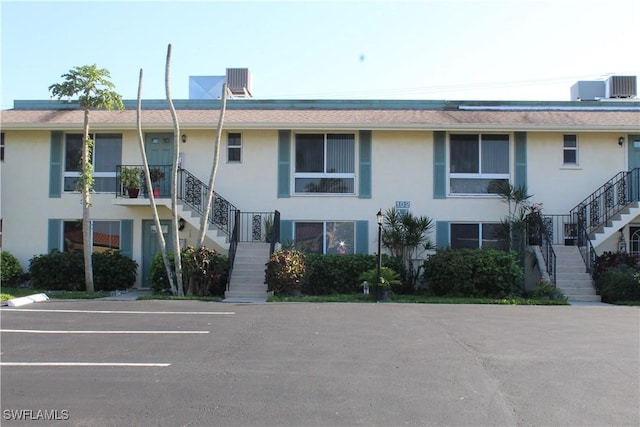 view of building exterior with stairs, uncovered parking, and central AC unit