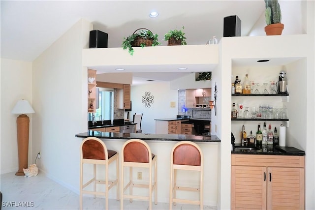 kitchen with a breakfast bar area, dark countertops, a sink, and backsplash