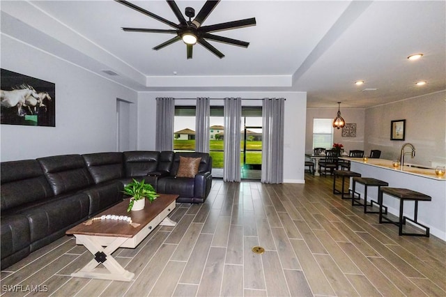 living area with a tray ceiling, recessed lighting, visible vents, ceiling fan with notable chandelier, and wood finished floors