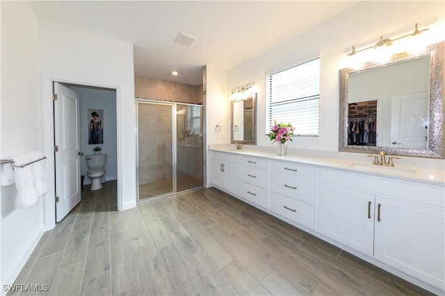 full bathroom with double vanity, toilet, wood finished floors, a sink, and a shower stall